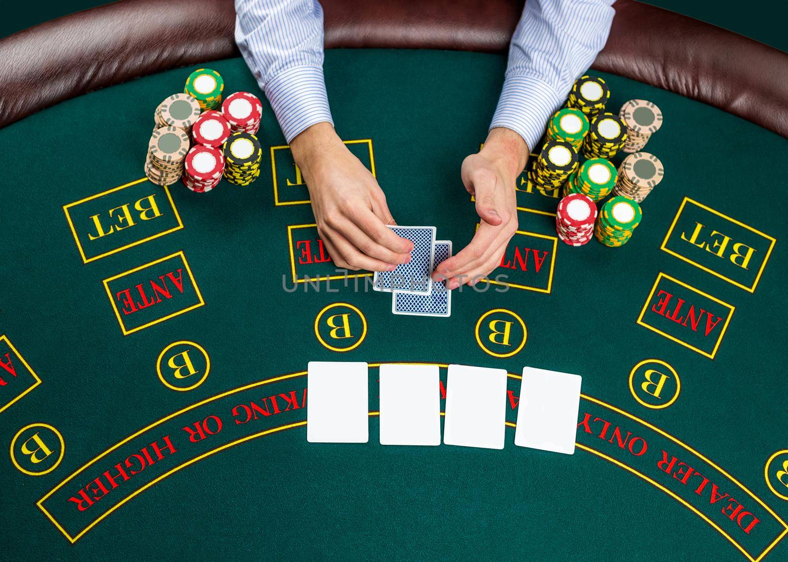 Close up of poker player with playing cards and chips at green casino table, view from above.