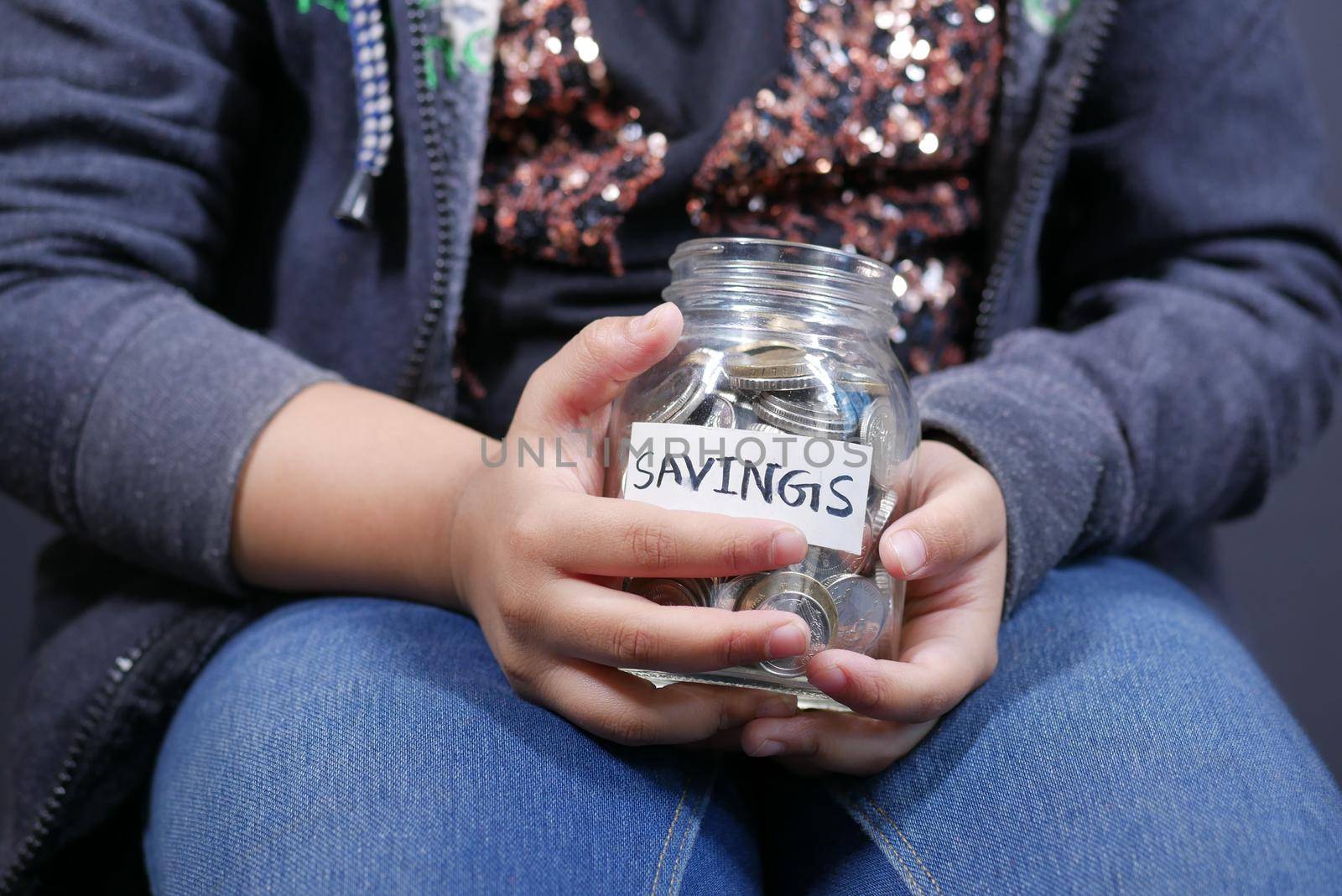 5 year old kid hand hold a saving coins jar .