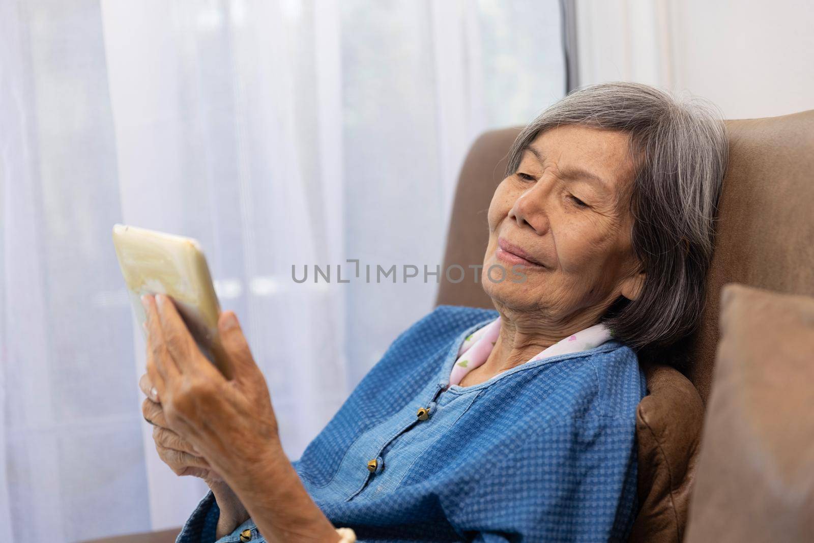 Elderly asian woman relax on couch in living room browsing wireless Internet on tablet by toa55