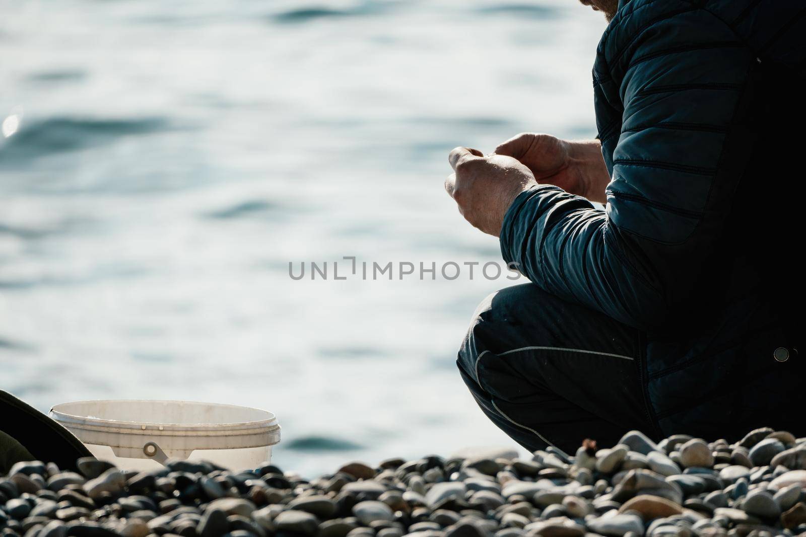 Man hobby fishing on sea tightens a fishing line reel of fish. Calm surface sea. Close-up of a fisherman hands twist reel with fishing line on a rod. Fishing in the blue sea outdoors. by panophotograph