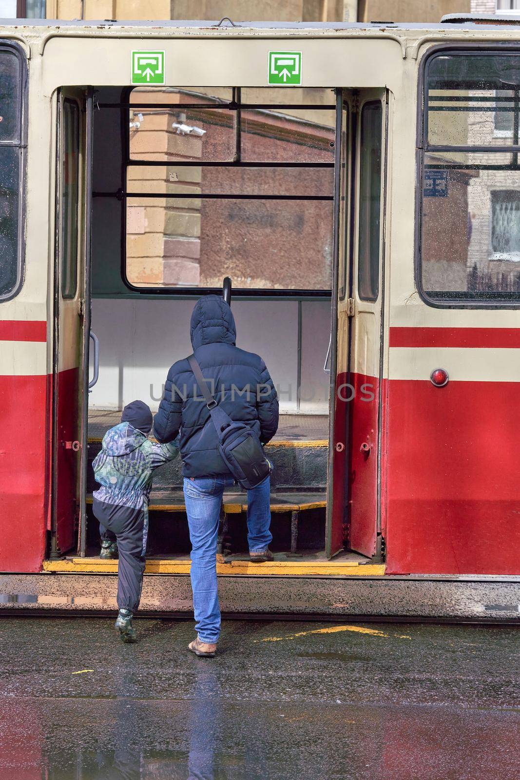 A man and a child walk through the open doors of public transport in the city by vizland