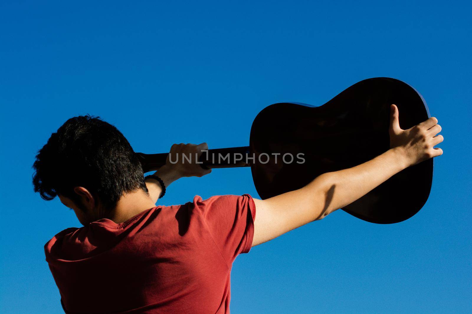 Young man rising an accoustic guitar in the sky by berkay