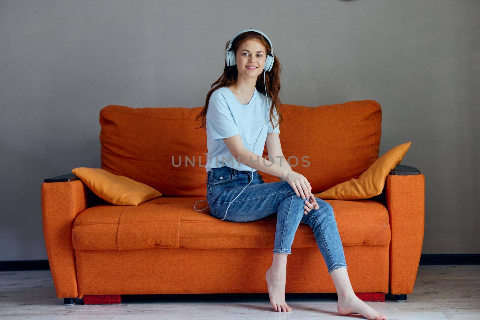 smiling woman sitting on the couch at home listening to music on headphones apartments. High quality photo