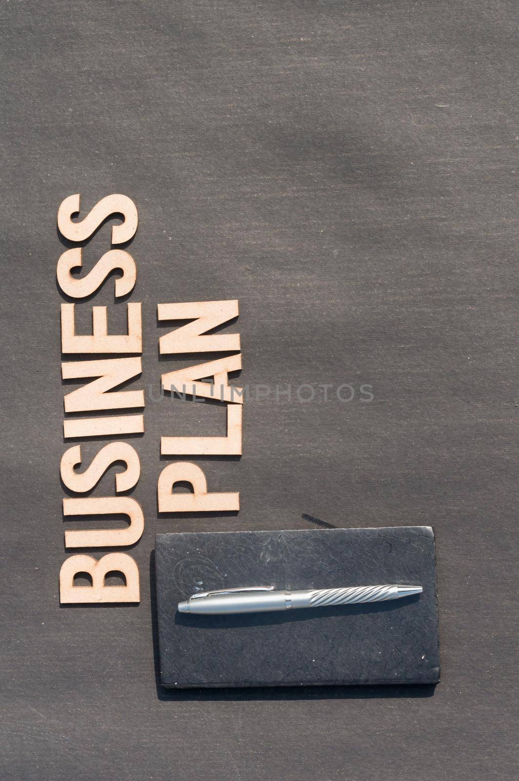 Businessman hand placing a pen and notebook in front of Word Business Plan made of wooden blocks of Alphabet letters. High Angle View. Vertical background. Close up