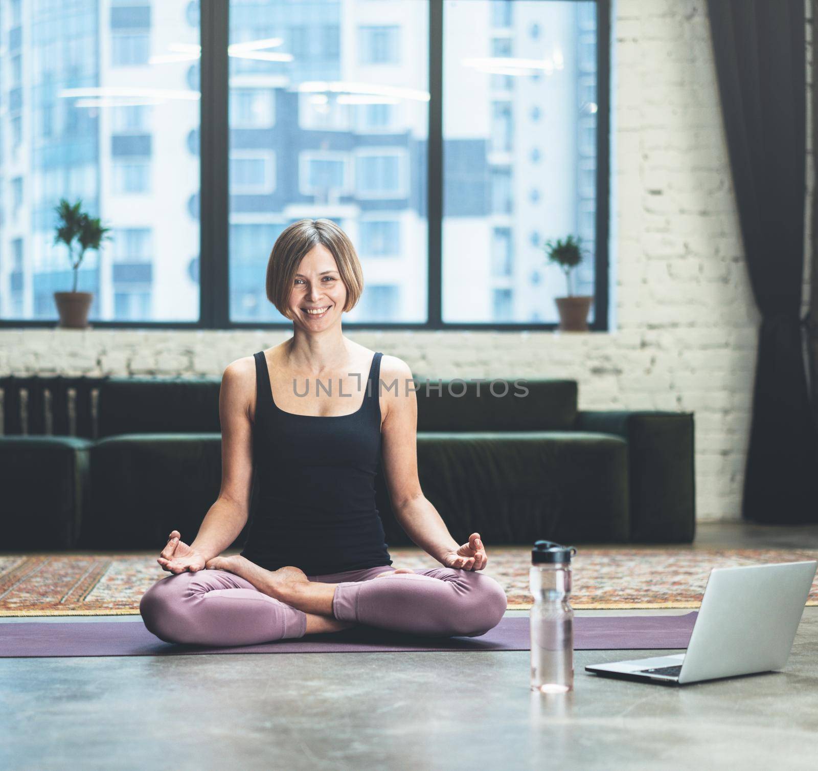 Woman Sitting in Lotus Pose and Meditating. She is Calm, relaxed and happy outside the window bustling metropolis. Yoga Female Practicing Yoga Meditation Exercise on the Mat in her Living Room at Home. Close-up