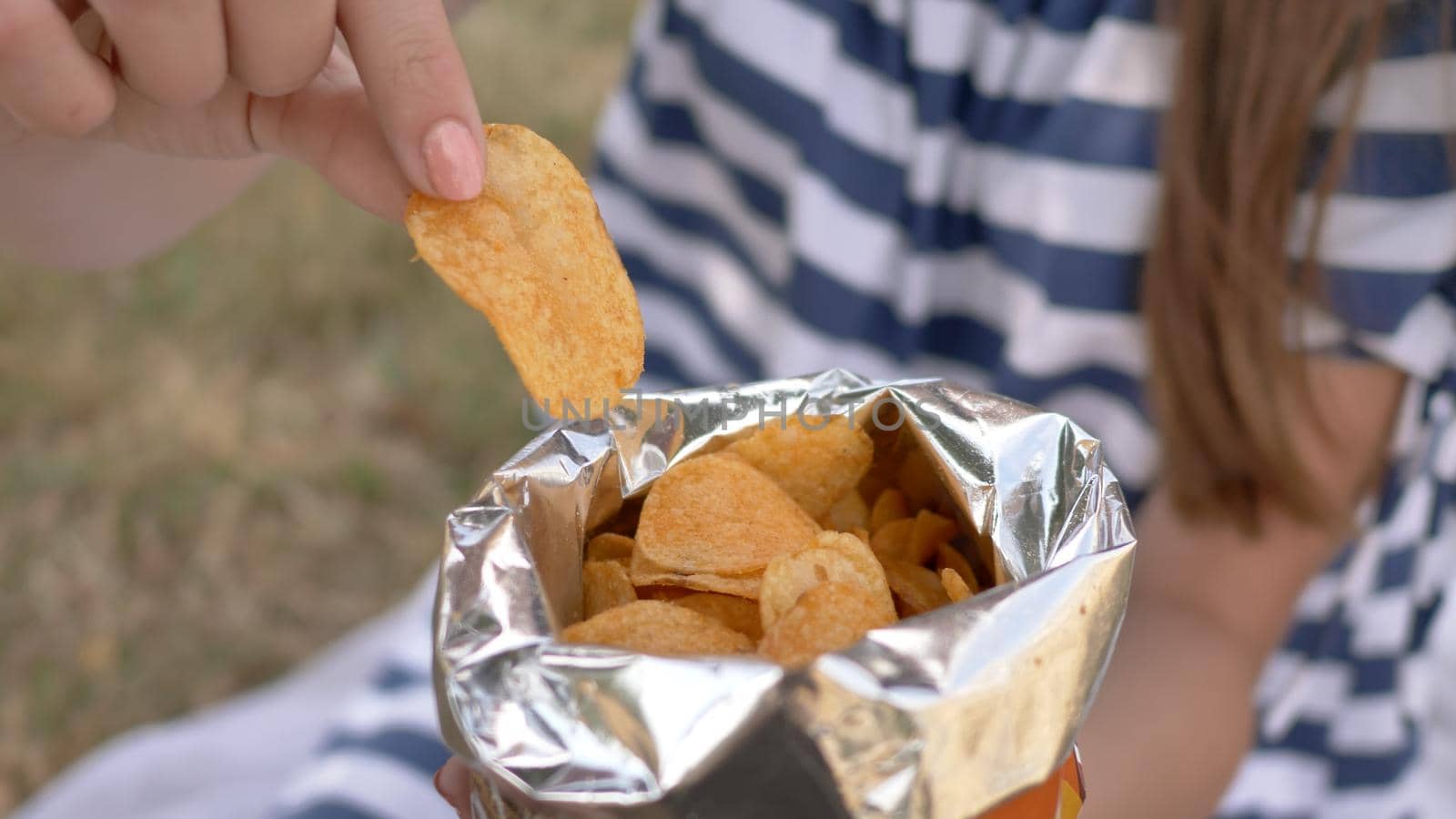 The girl eats chips in the city park in the summer. The girl eats chips in the city park in the summer. Package with chips close-up