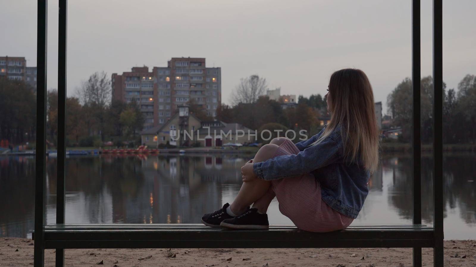 A lonely young girl sits on a bench in the city on an autumn evening. by DovidPro