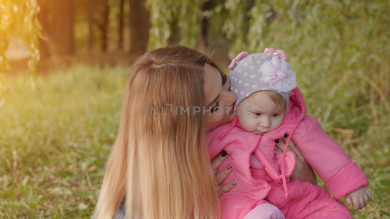 Happy young mother with her baby is sitting on the grass in the park in the autumn evening