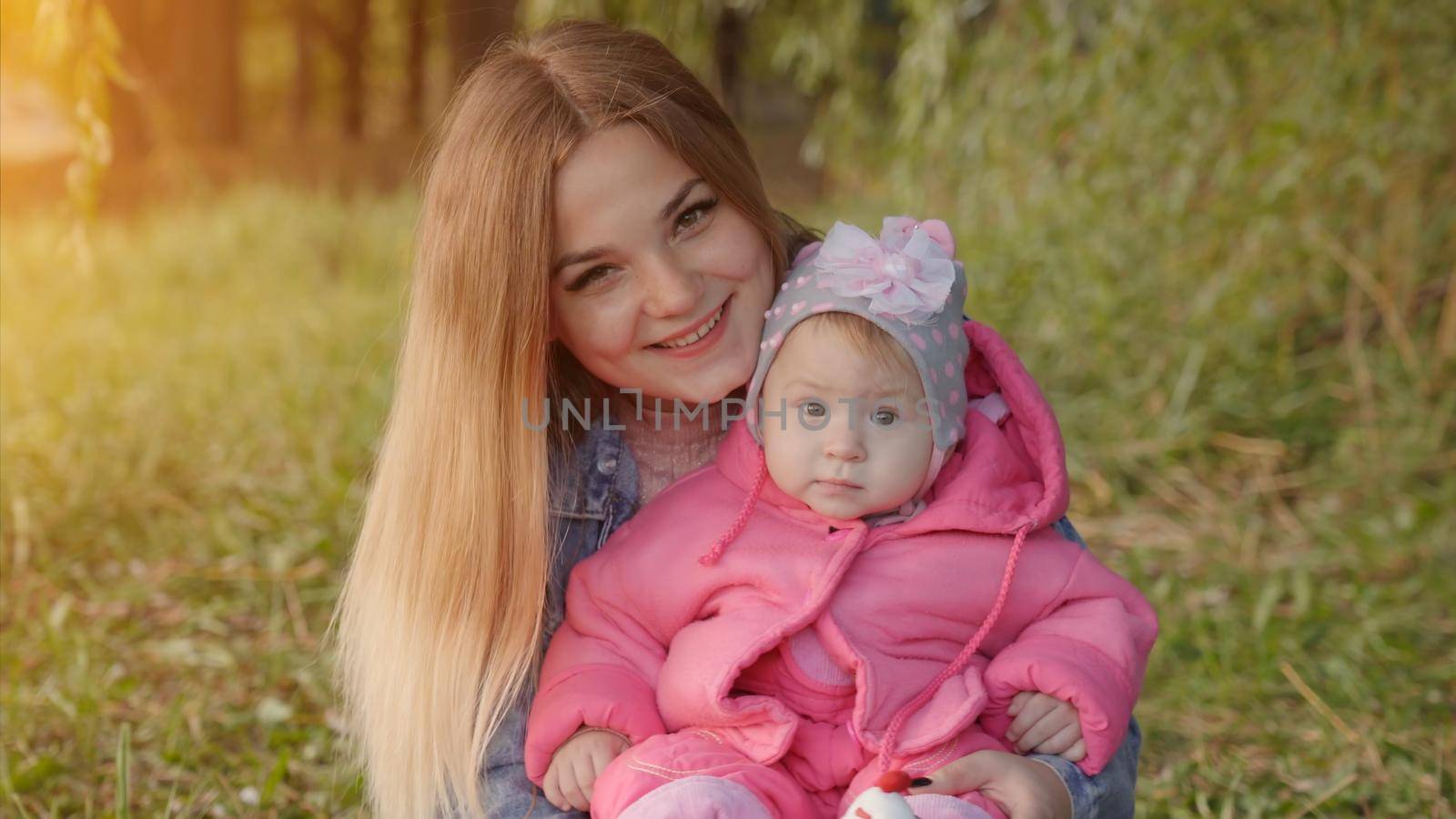 Happy young mother with her baby is sitting on the grass in the park in the autumn evening. by DovidPro