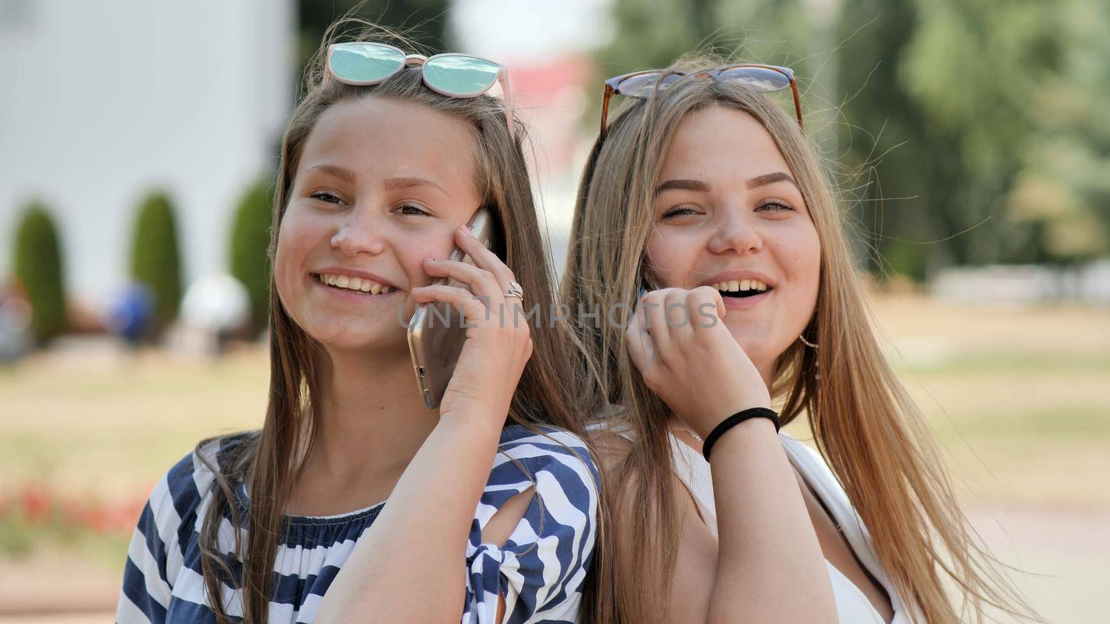 Two young girls talking on the phone on a summer day. by DovidPro