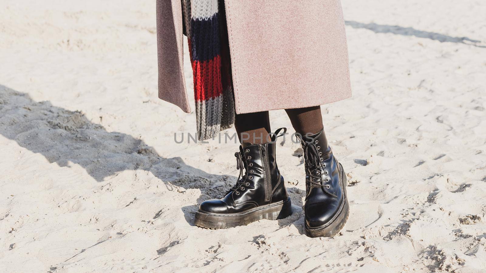 Stylish black smooth leather ankle boots in outdoor on the sand beach. Cold season outfit