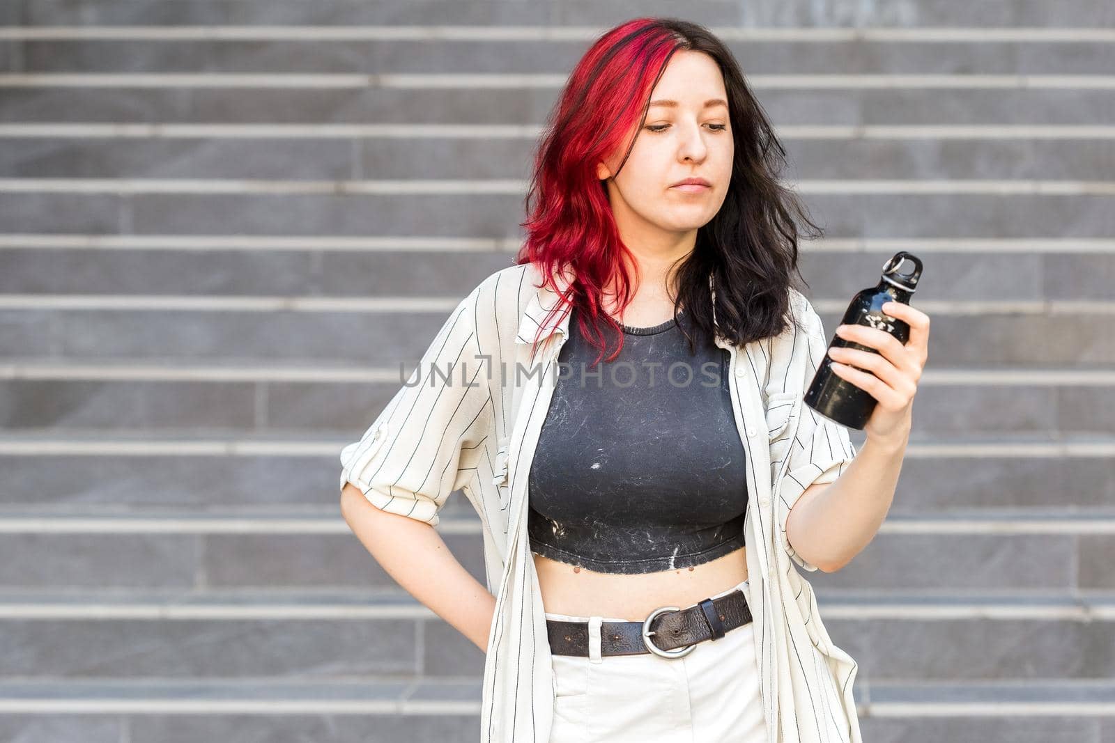 Portrait of young stylish woman with steel eco bottle in hand, wearing casual clothes