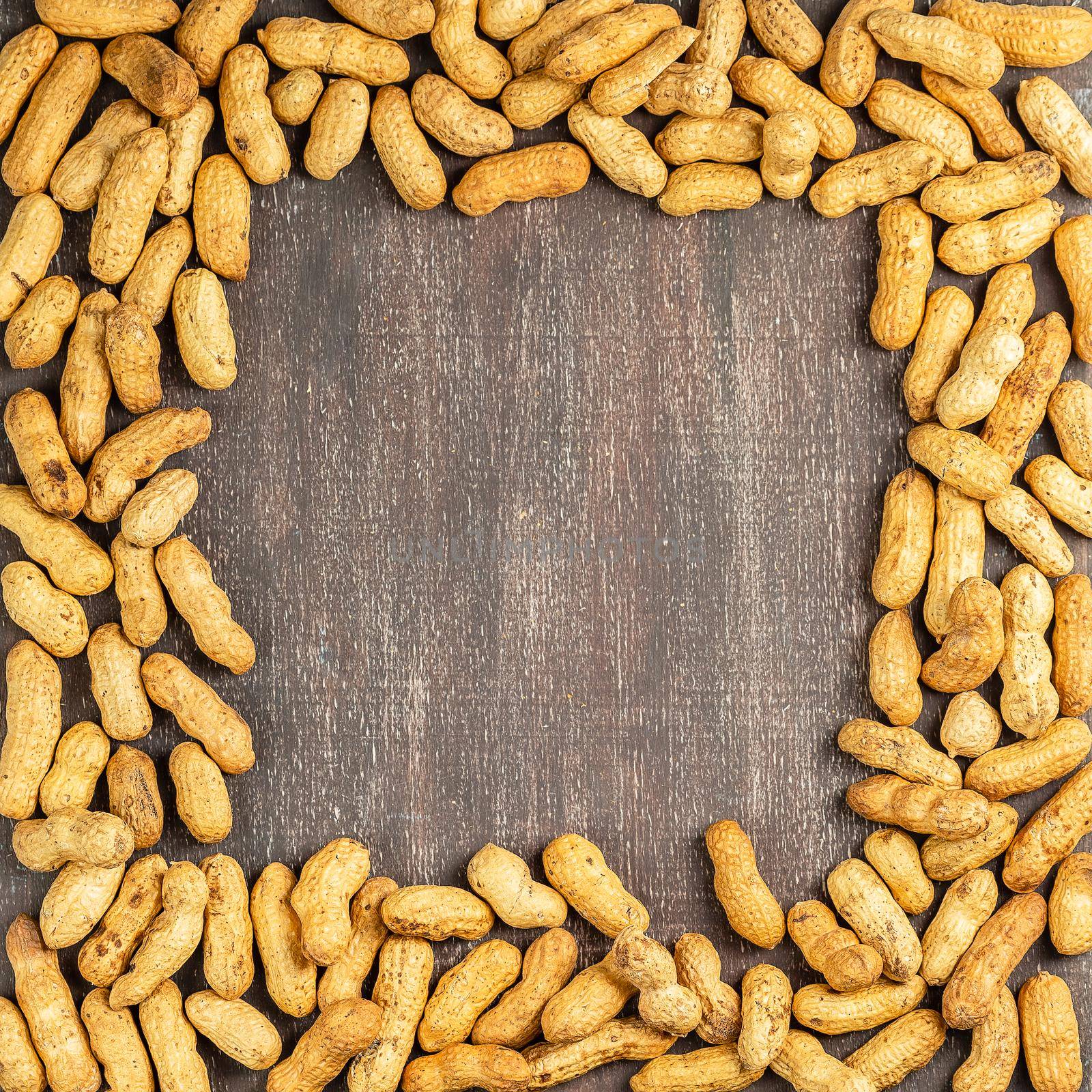 Square frame of the shelled peanuts. Not peeled groundnuts border - top view on wooden background