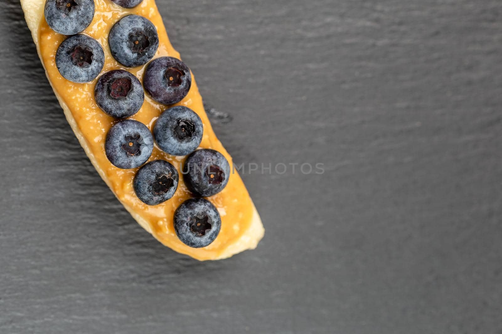 Healthy appetizers with sliced bananas with peanut butter spread and blueberries on the top on the slate plate, space for text