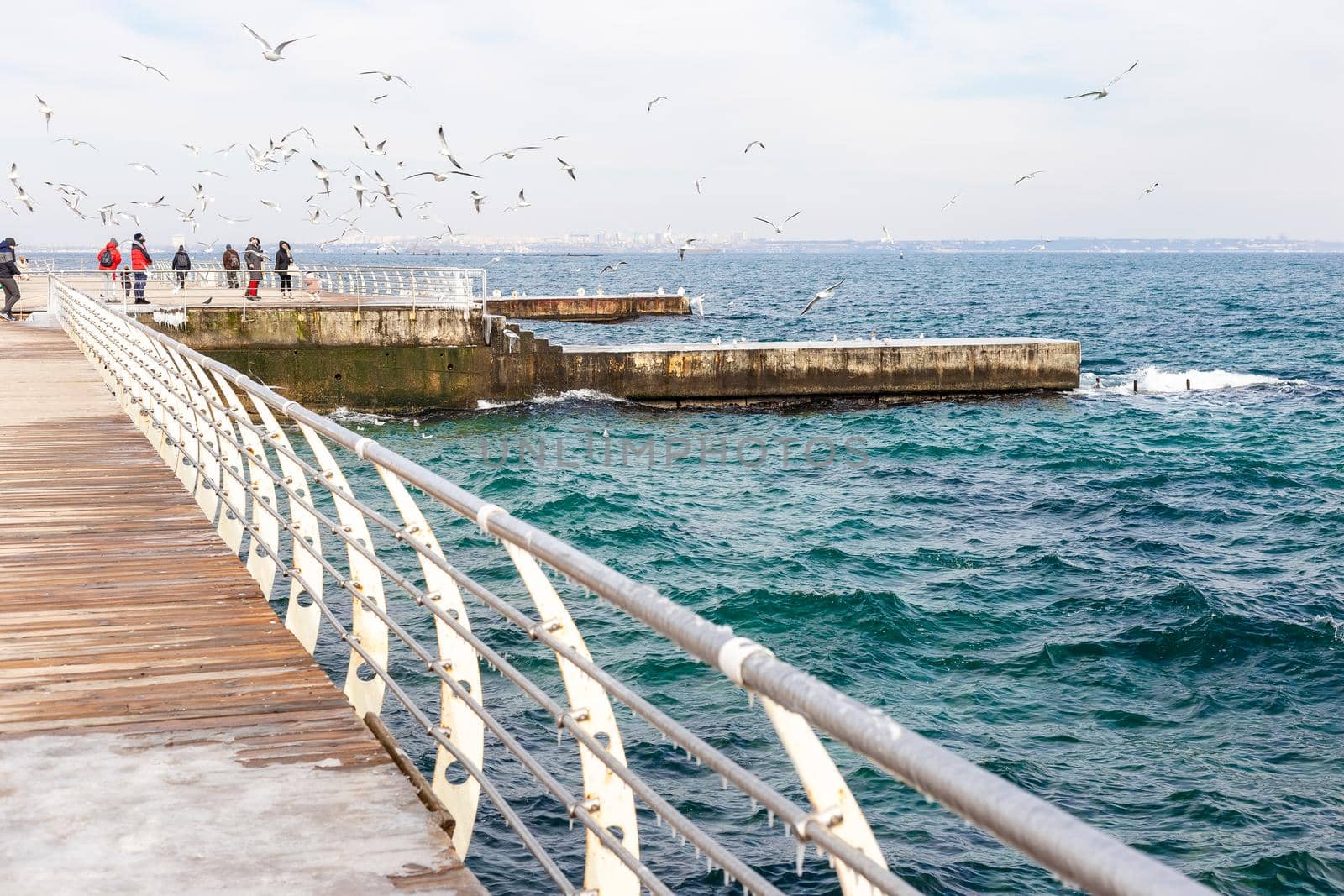 Odessa, Ukraine - February 19, 2021. People are walking on the pier feeding seagulls. Black Sea in winter, Langeron quay in Odessa city, Ukraine