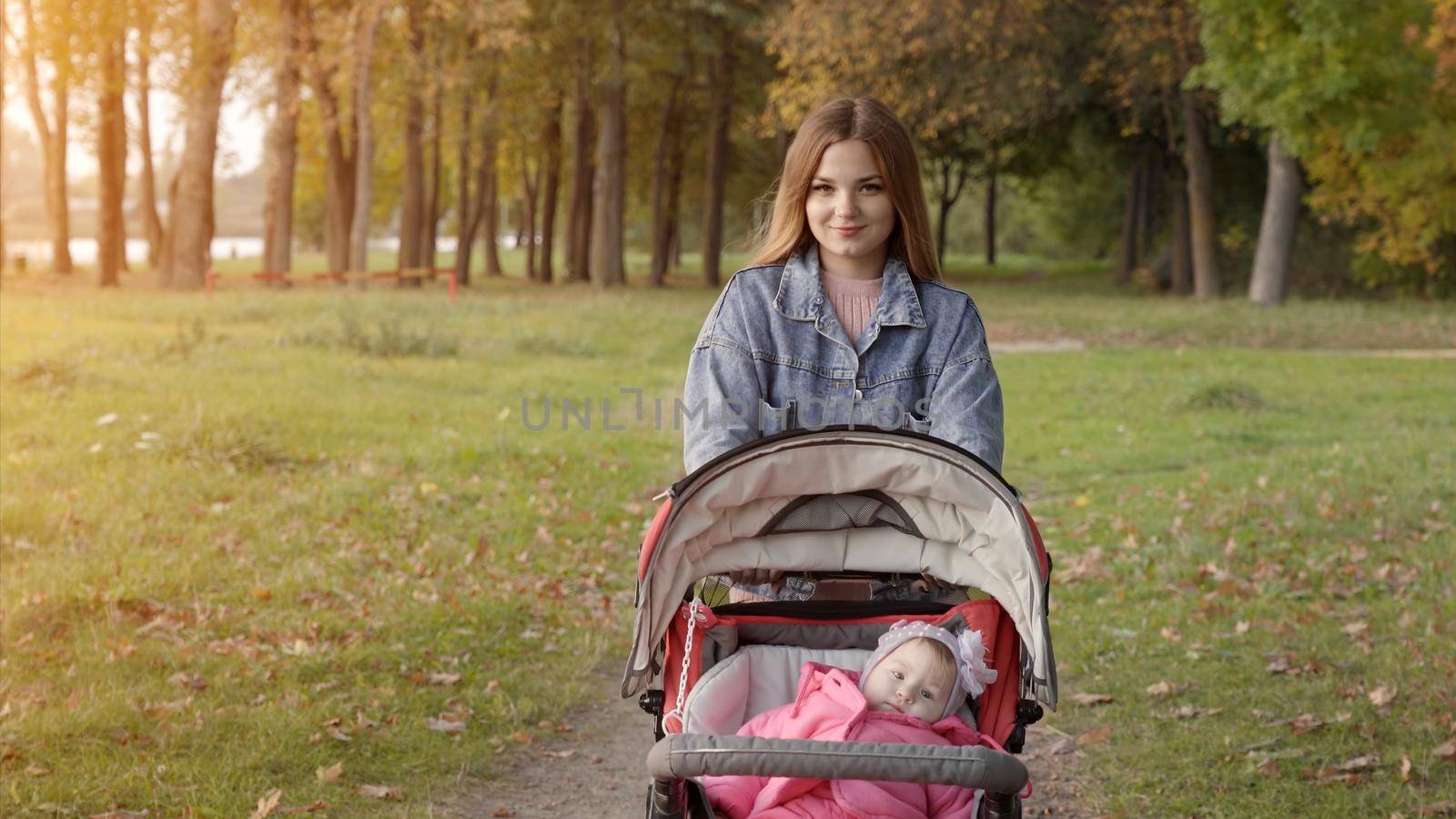 A young mother with a stroller walks in the autumn evening
