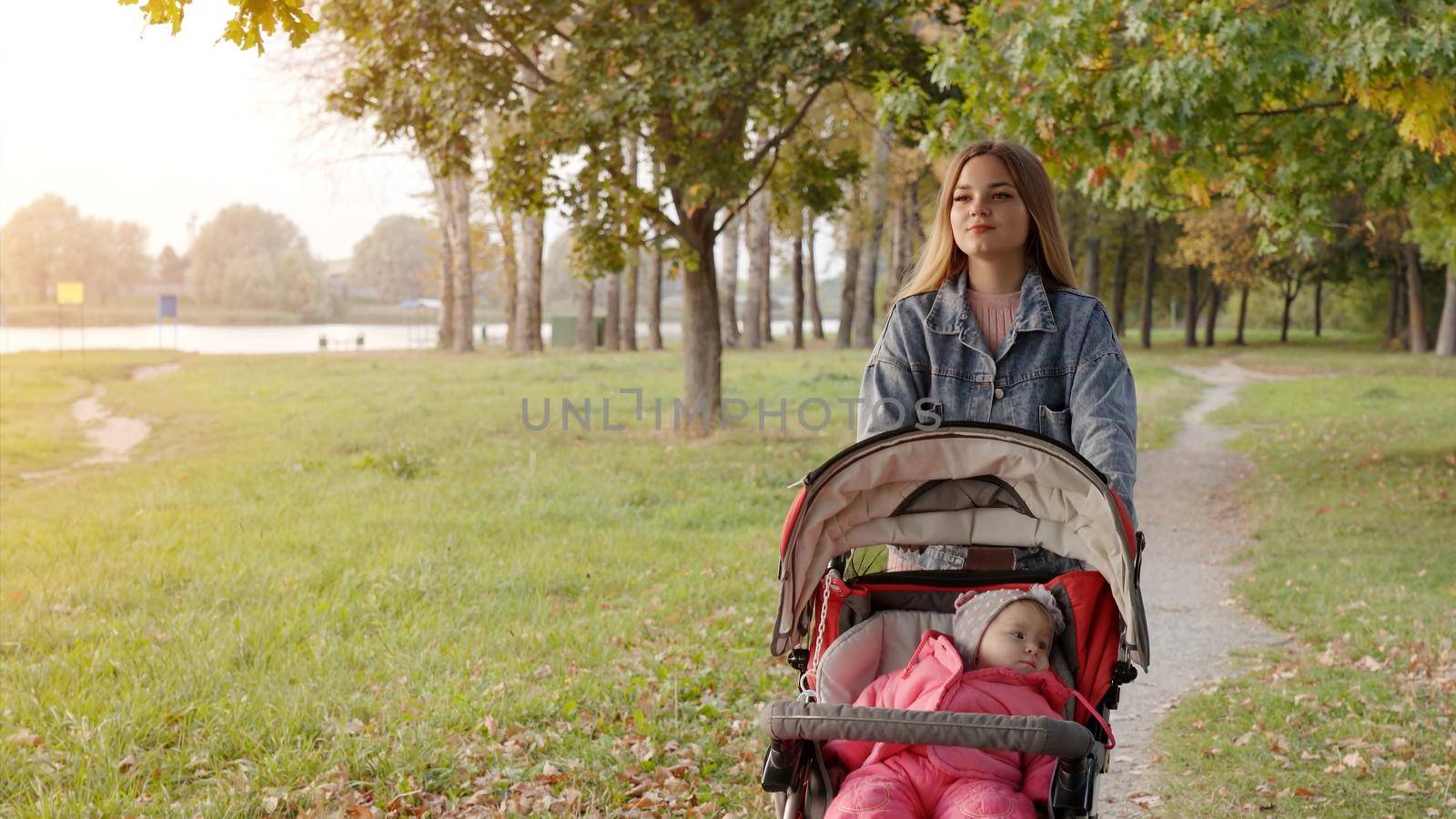 A young mother with a stroller walks in the autumn evening