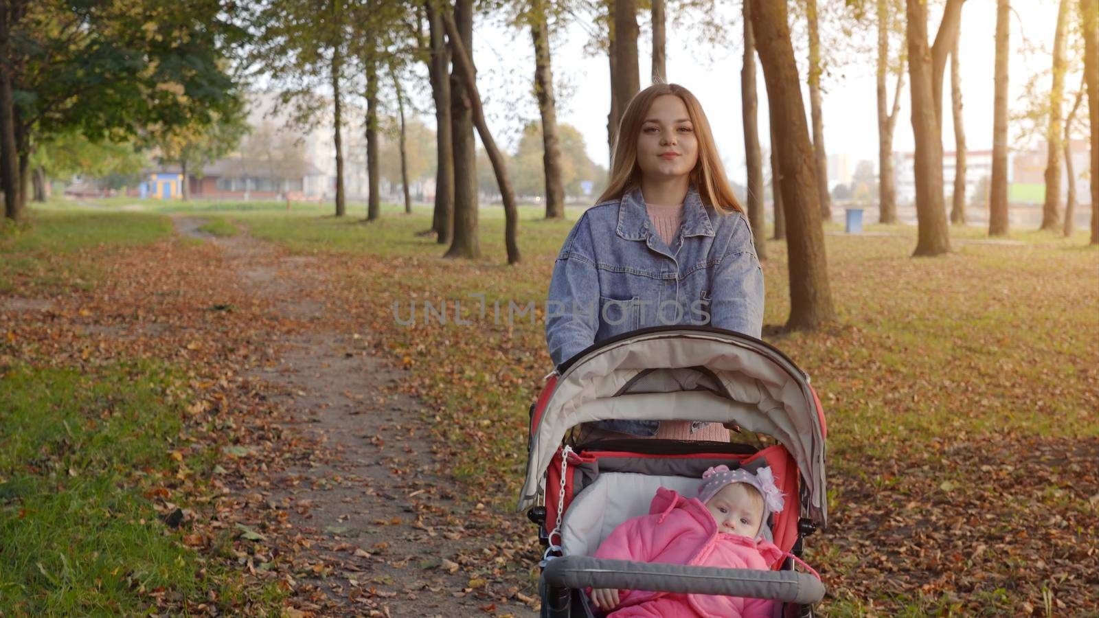 A young mother with a stroller walks in the autumn evening