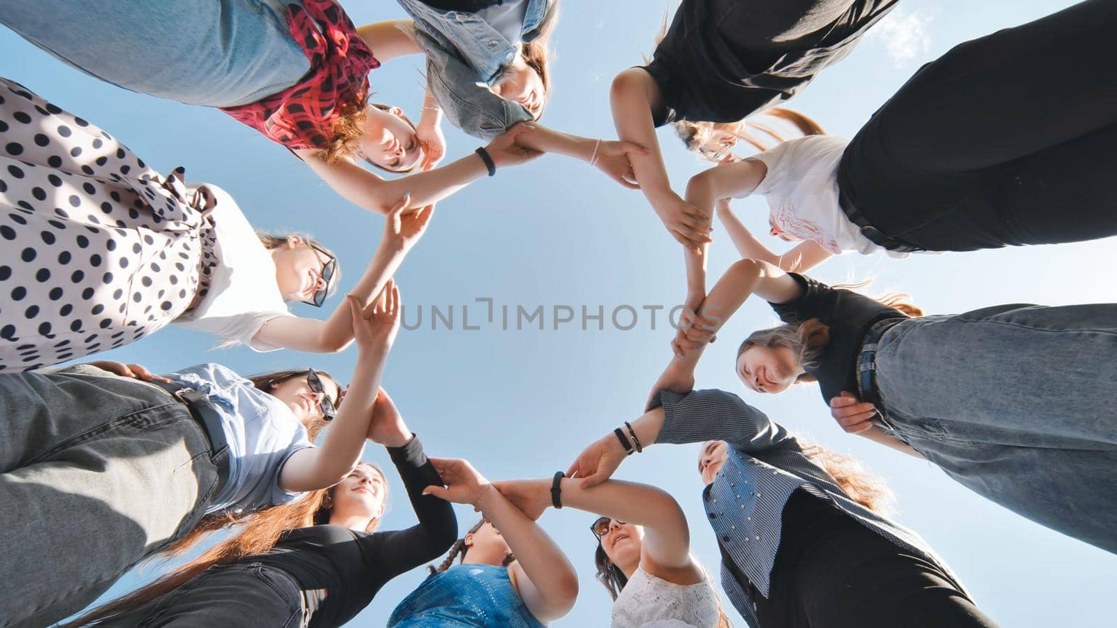 A group of girls makes a circle shape holding each other's hands. by DovidPro