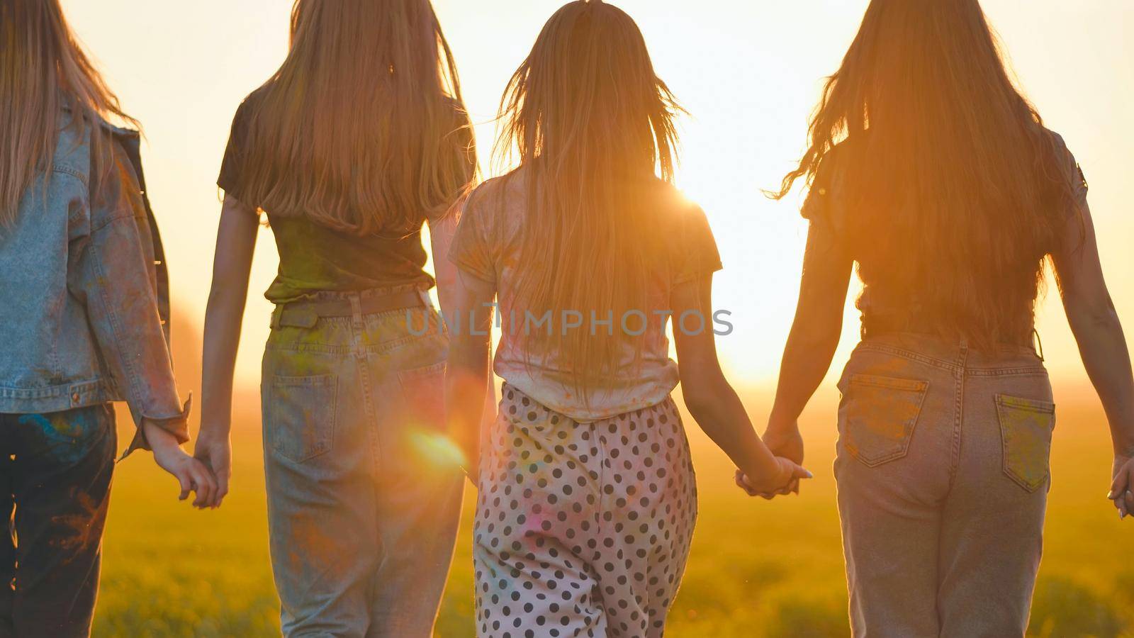 A group of girls walk towards the sun at sunset holding hands. by DovidPro