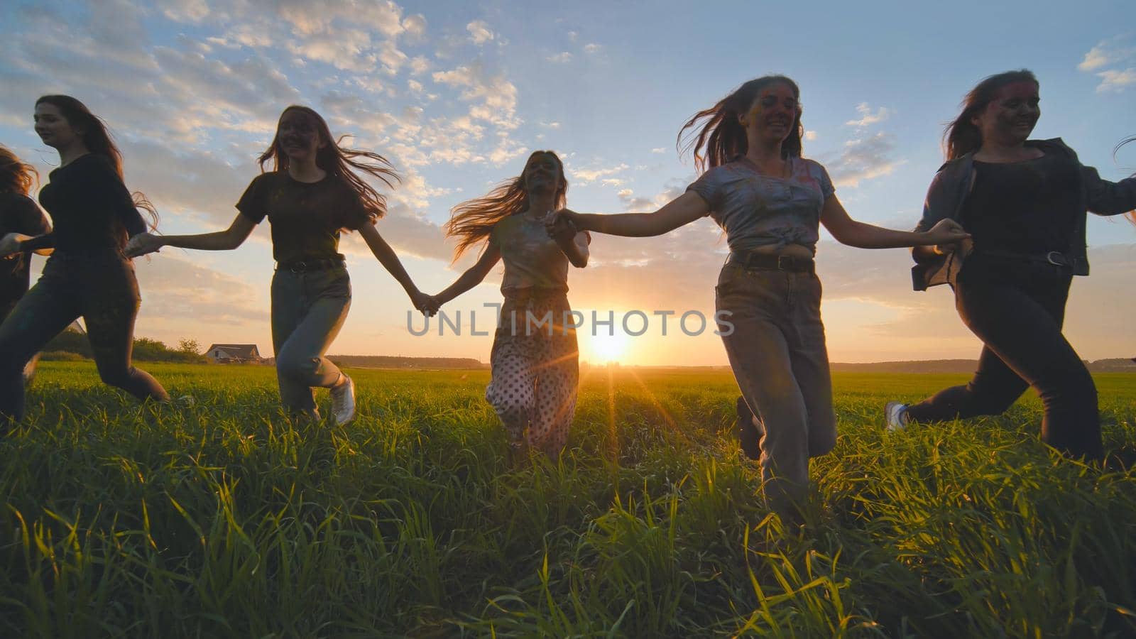 Eleven cheerful girls run to the meeting across the field in the summer, holding hands