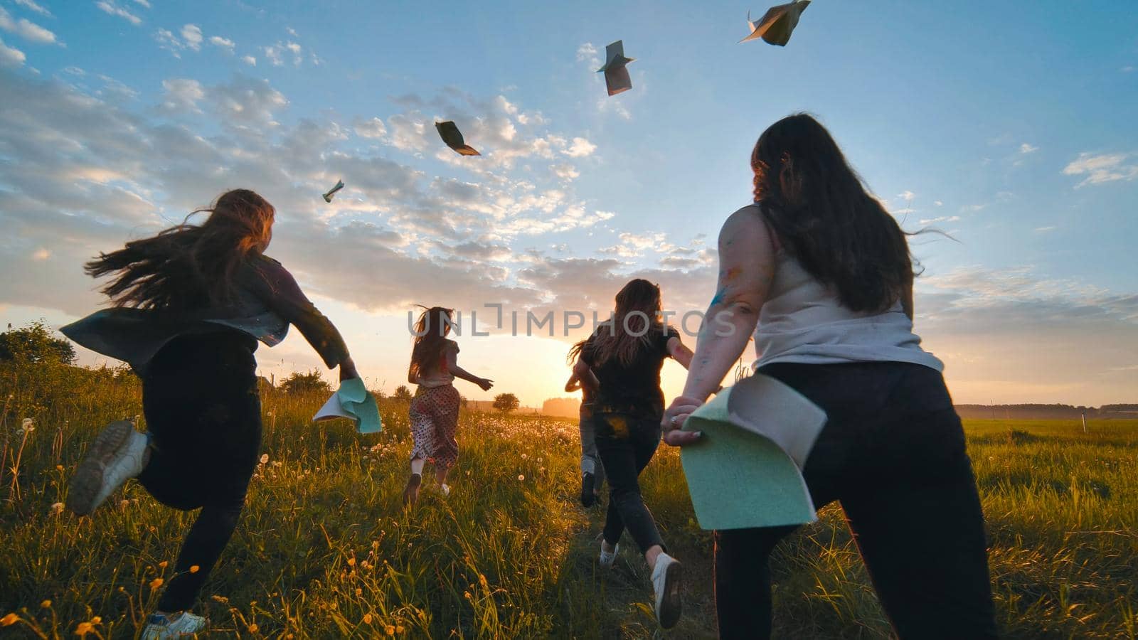 Cheerful students run throwing notebooks after school at sunset. by DovidPro