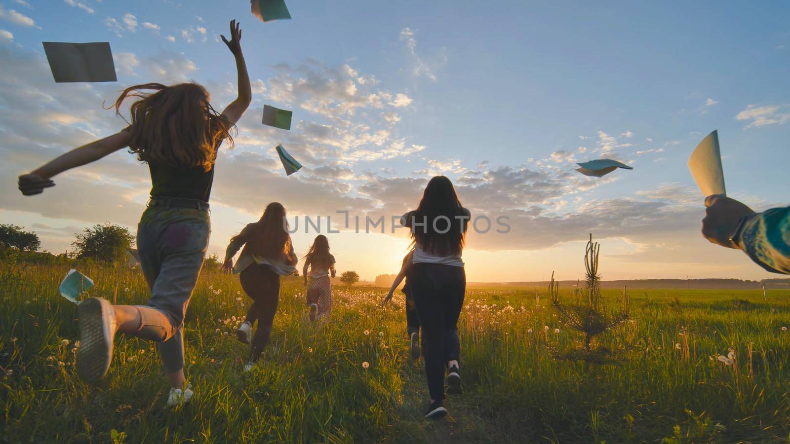 Cheerful students run throwing notebooks after school at sunset. by DovidPro