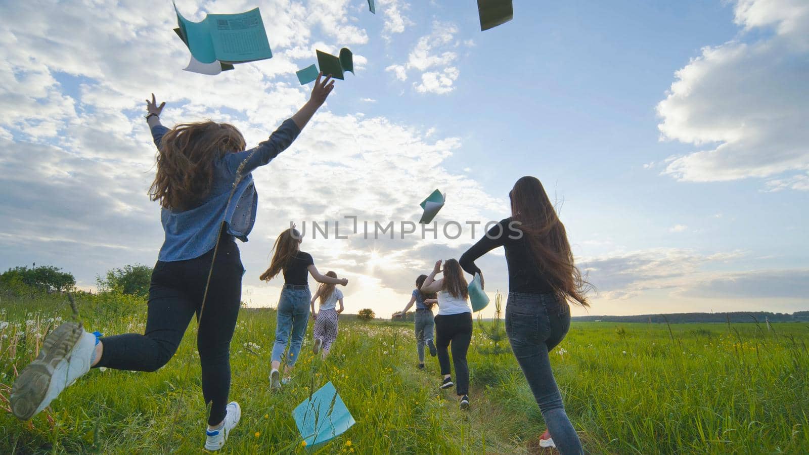 Cheerful students run throwing notebooks after school at sunset. by DovidPro