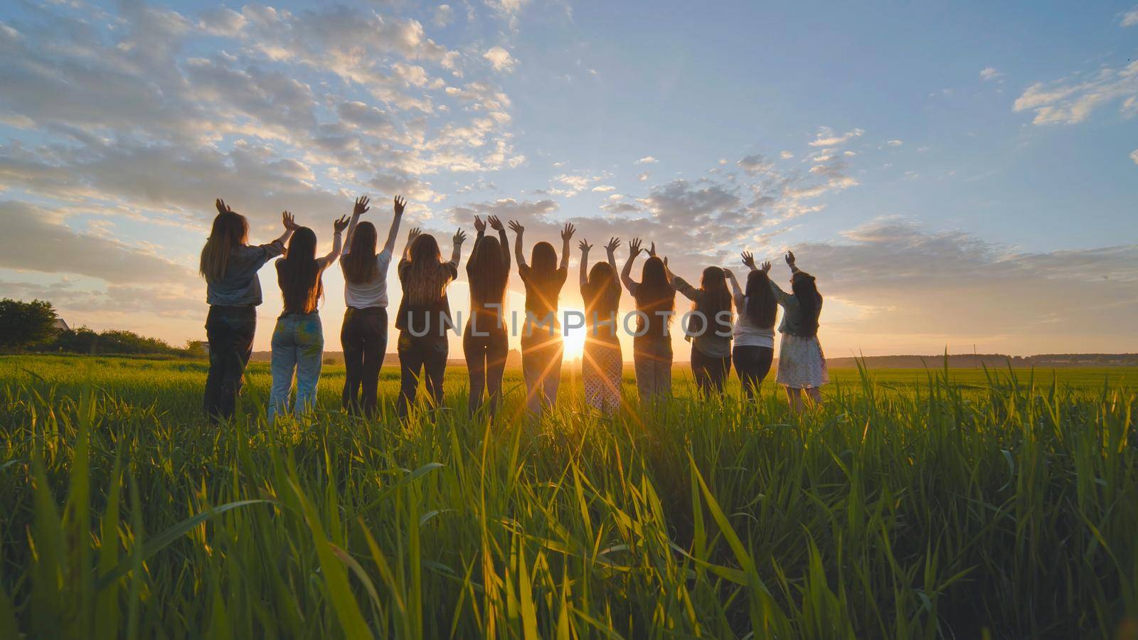 Silhouette of friends of 11 girls waving their hands at sunset in the field. by DovidPro