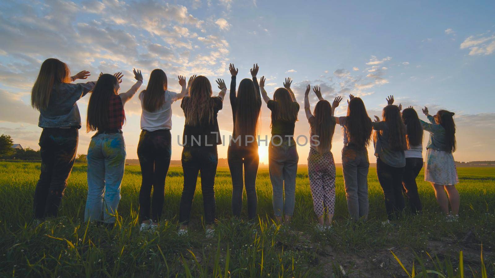 Silhouette of friends of 11 girls waving their hands at sunset in the field. by DovidPro