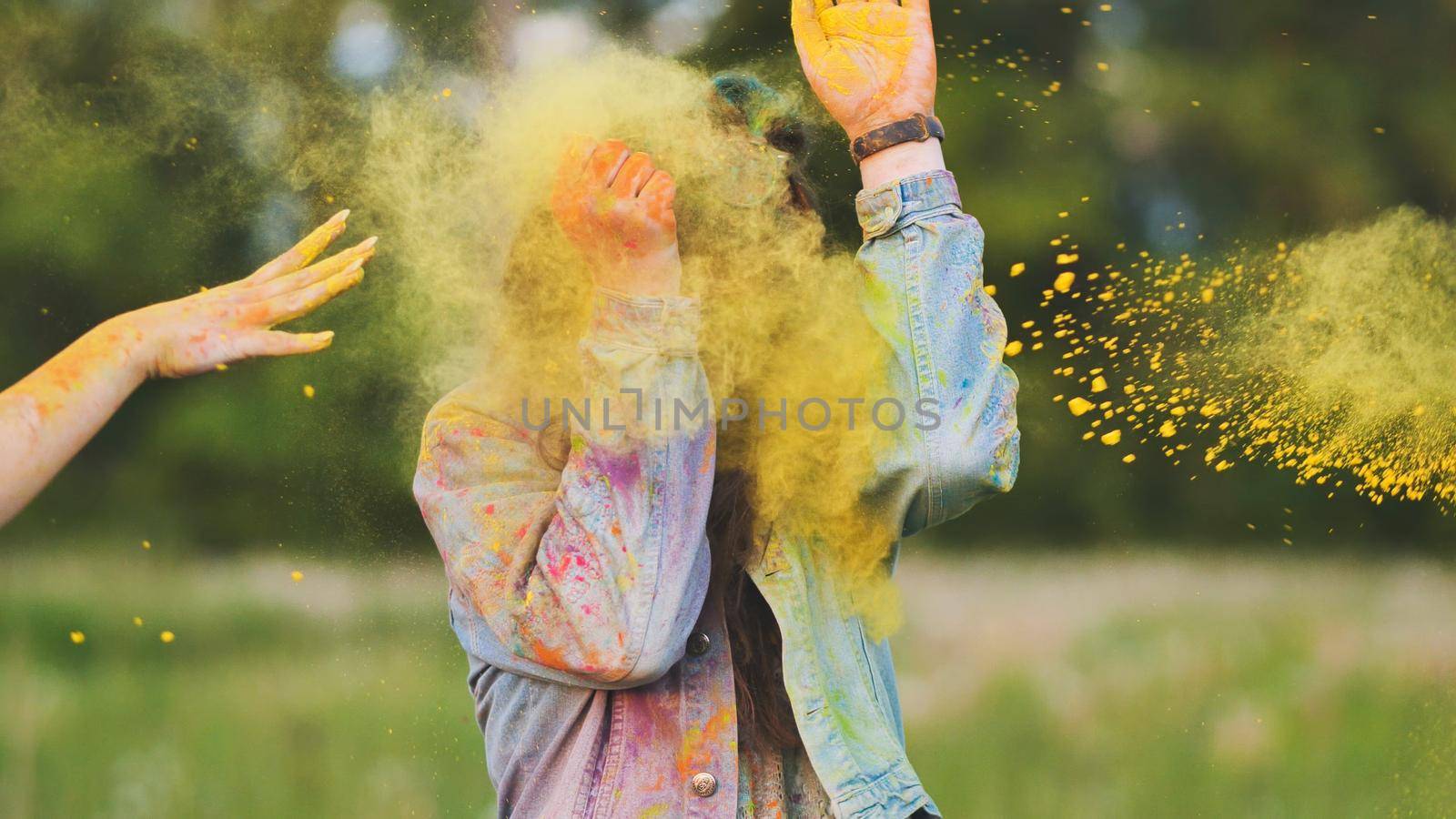 Friends sprinkle their cheerful girlfriend with multi-colored powder. Holi holiday