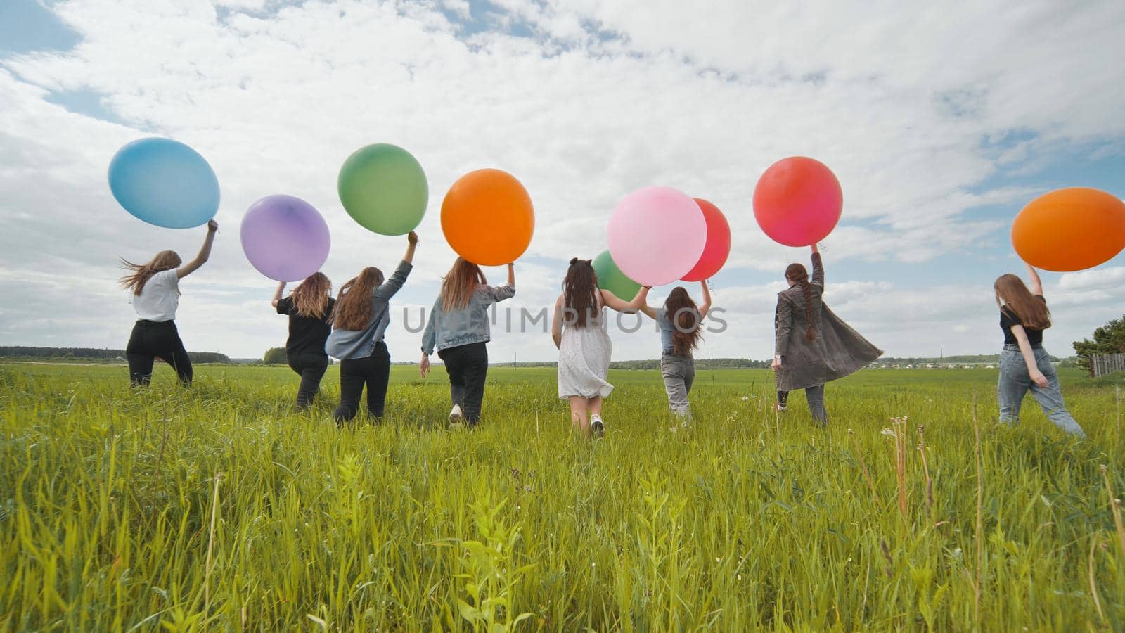 Girls friends are walking across the field with large balloons and colorful balloons