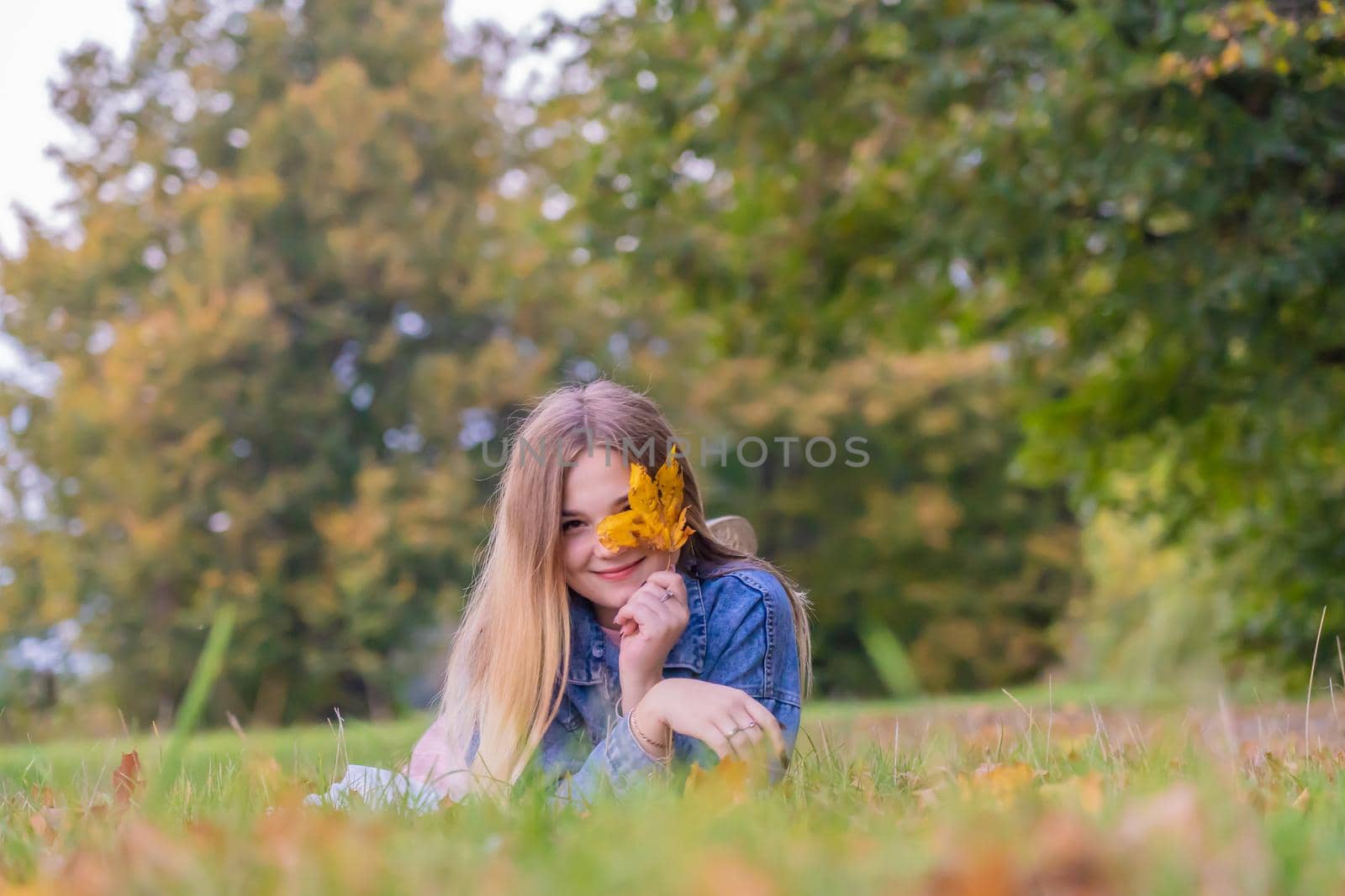 A young girl lies on the grass in a warm autumn in the evening with a petal in her hands
