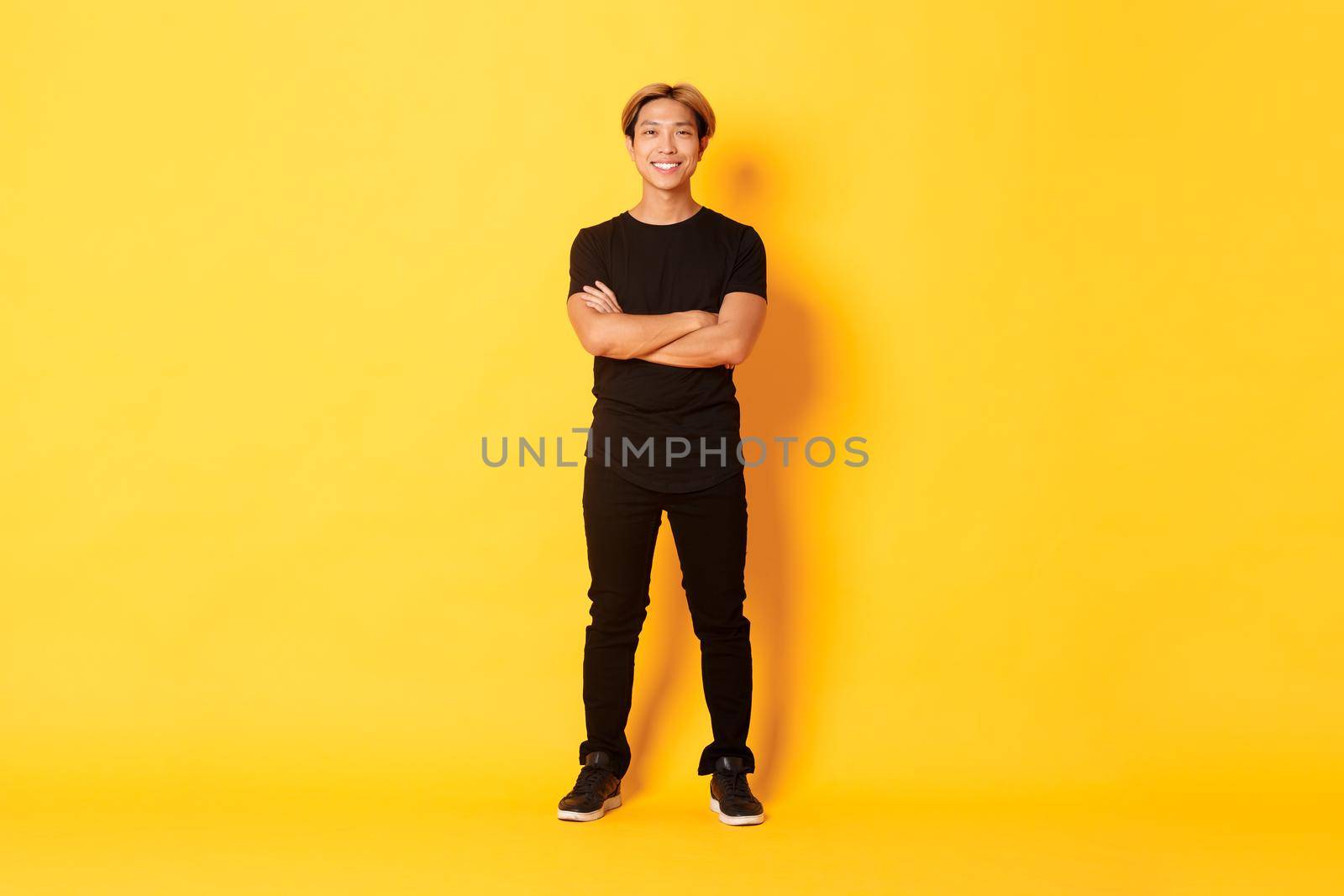 Full length of smiling confident asian blong guy, cross arms chest over yellow background.