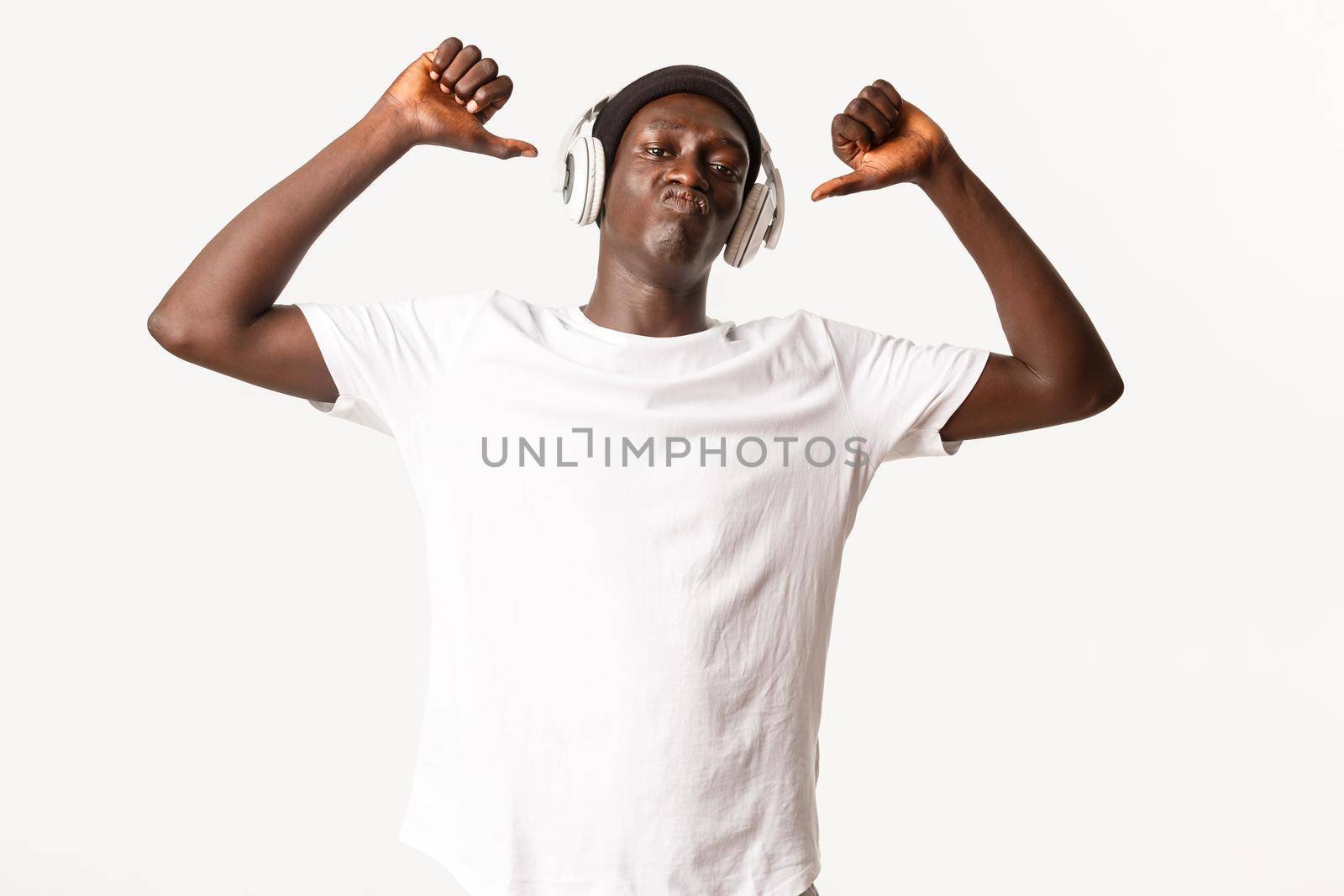 Portrait of happy and proud african-american young male, pointing fingers at himself to show-off, pouting sassy, white background by Benzoix