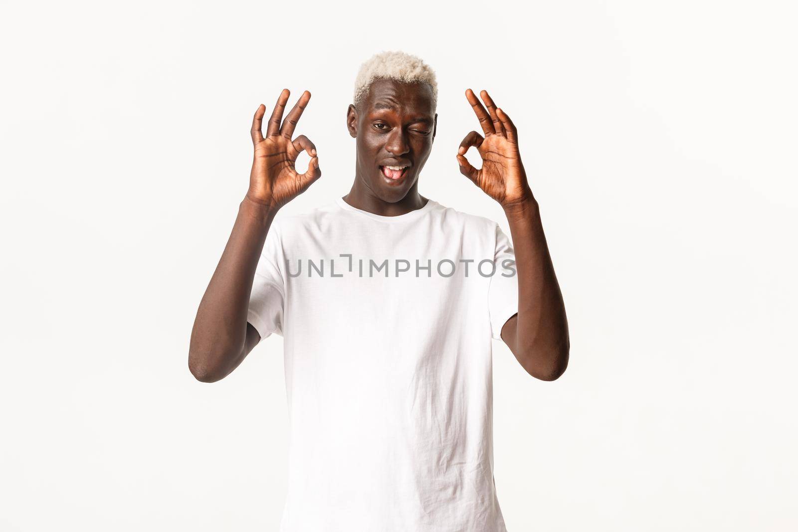 Portrait of sassy attractive african-american blond man, winking and showing okay gesture in approval, standing white background.