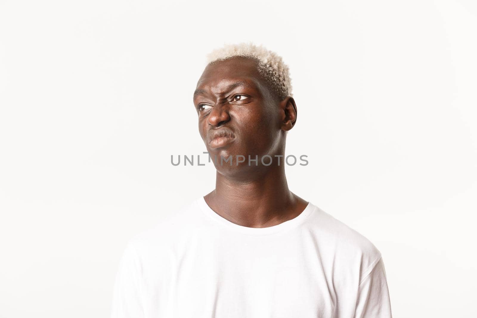 Close-up of skeptical and displeased african-american blond guy, looking left and grimacing disappointed, dislike something, standing white background by Benzoix