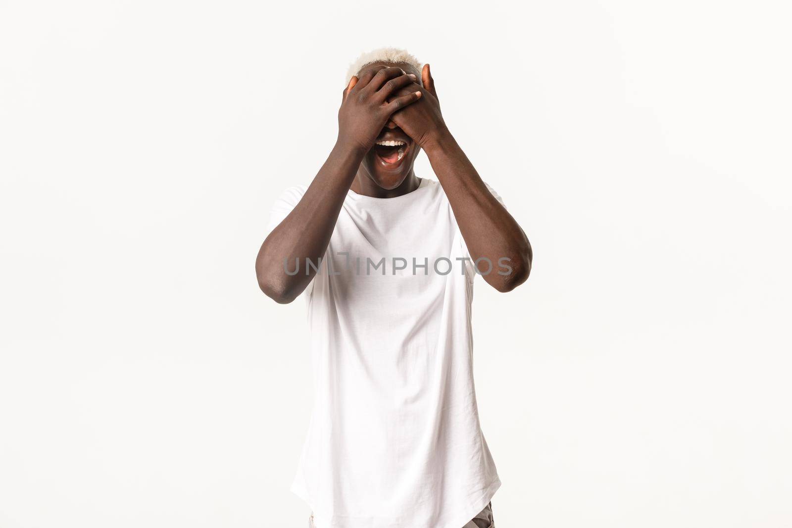 Portrait of surprised and amused african-american blond guy, shut eyes with hands and smiling amazed, white background by Benzoix