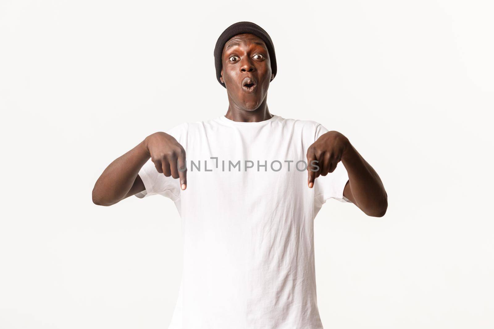 Portrait of impressed and excited african-american handsome guy pointing fingers down, gasping astonished, white background by Benzoix