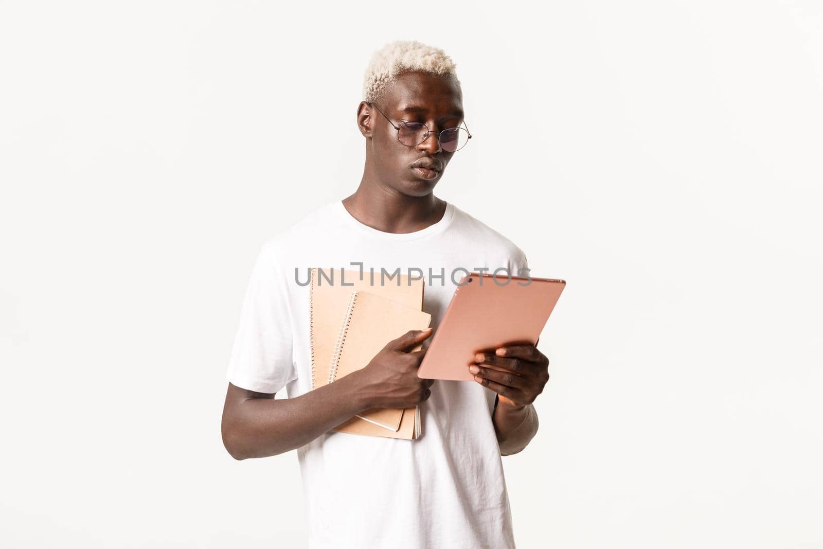 Portrait of determined, serious-looking african american male student, looking focused at digital tablet, studying, holding notebooks, standing white background by Benzoix