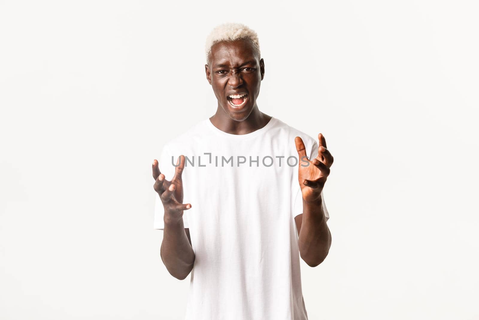 Portrait of mad african-american blond man, clenching hands and swearing, shouting angry, looking furious over white background.