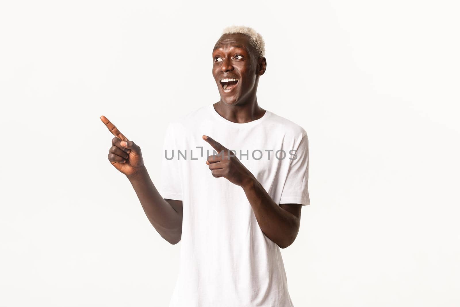 Portrait of excited handsome african-american blond guy, looking happy and surprised at logo, pointing fingers upper left corner, white background by Benzoix