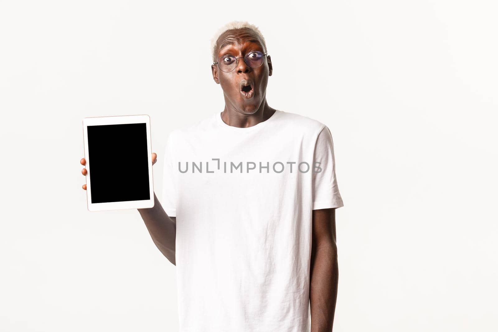 Portrait of impressed and wondered stylish african-american guy in glasses, open mouth fascinated and showing digital tablet screen, amazing app, white background.