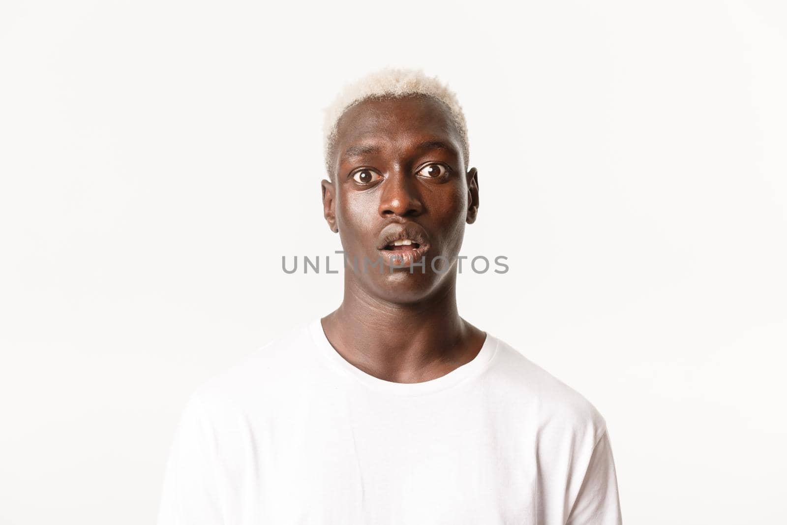 Close-up of startled gasping african-american blond man, drop jaw and looking wondered at camera, standing white background.