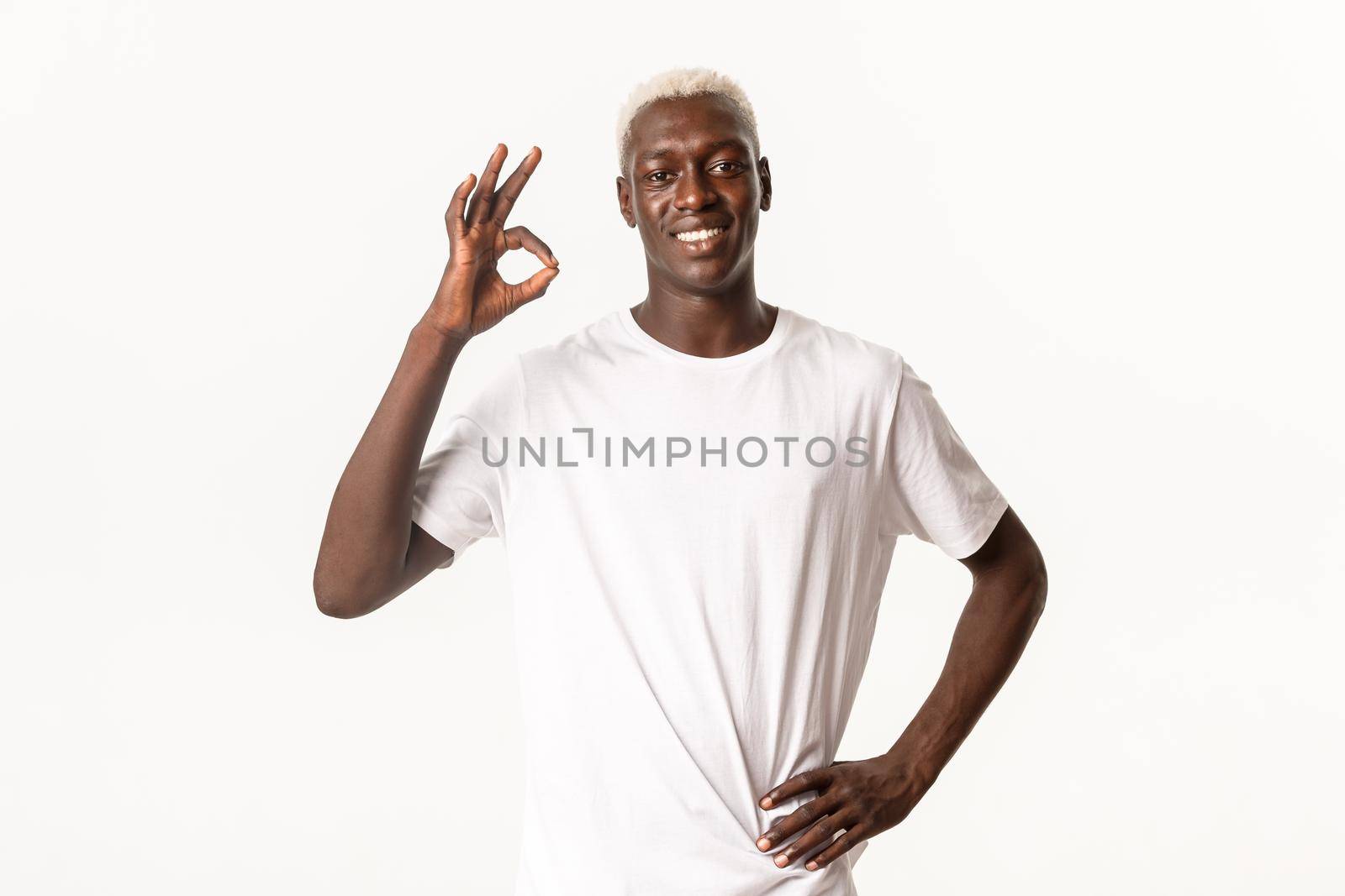 Portrait of satisfied african-american blond man, showing approval okay gesture and smiling, standing white background.