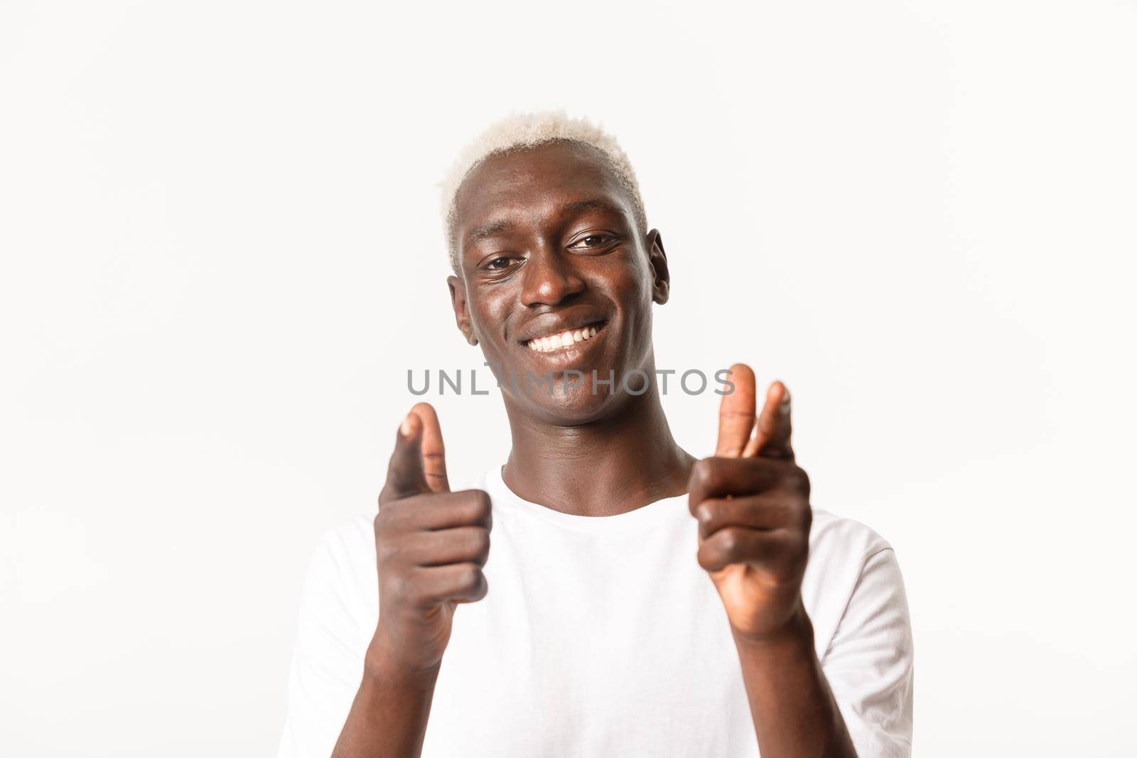 Close-up of supportive handsome african-american blond guy pointing fingers at camera and smiling, congratulating, praising good choice, standing over white background.