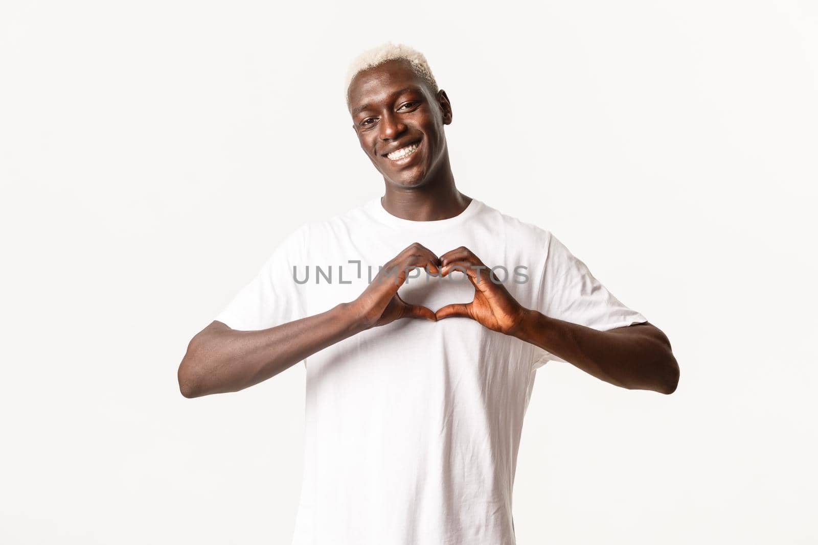 Portrait of lovely african-american blond guy, smiling happy and showing heart gesture, white background.