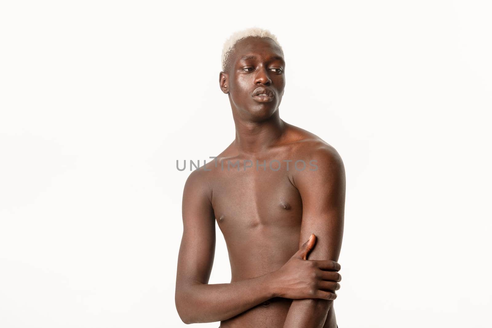 Portrait of sensual handsome african-american blond male model, standing naked chest and looking aside thoughtful, posing over white background.