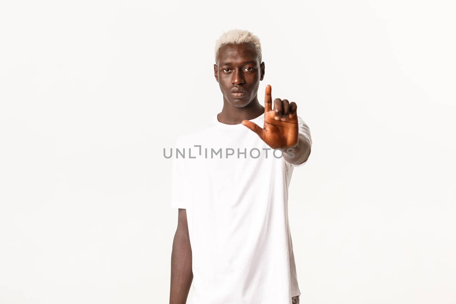 Portrait of serious african-american young handsome man, extend hand and showing finger, stop or disapprove something, dislike offer, scolding person, white background.