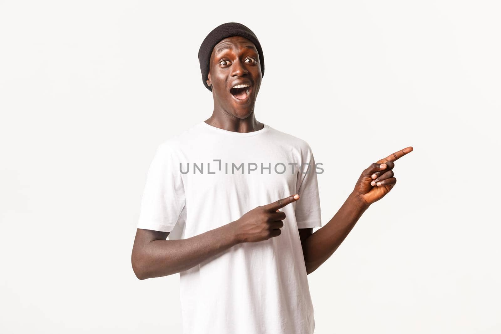 Portrait of amused handsome african-american guy, open mouth wondered and pointing fingers right, standing white background.